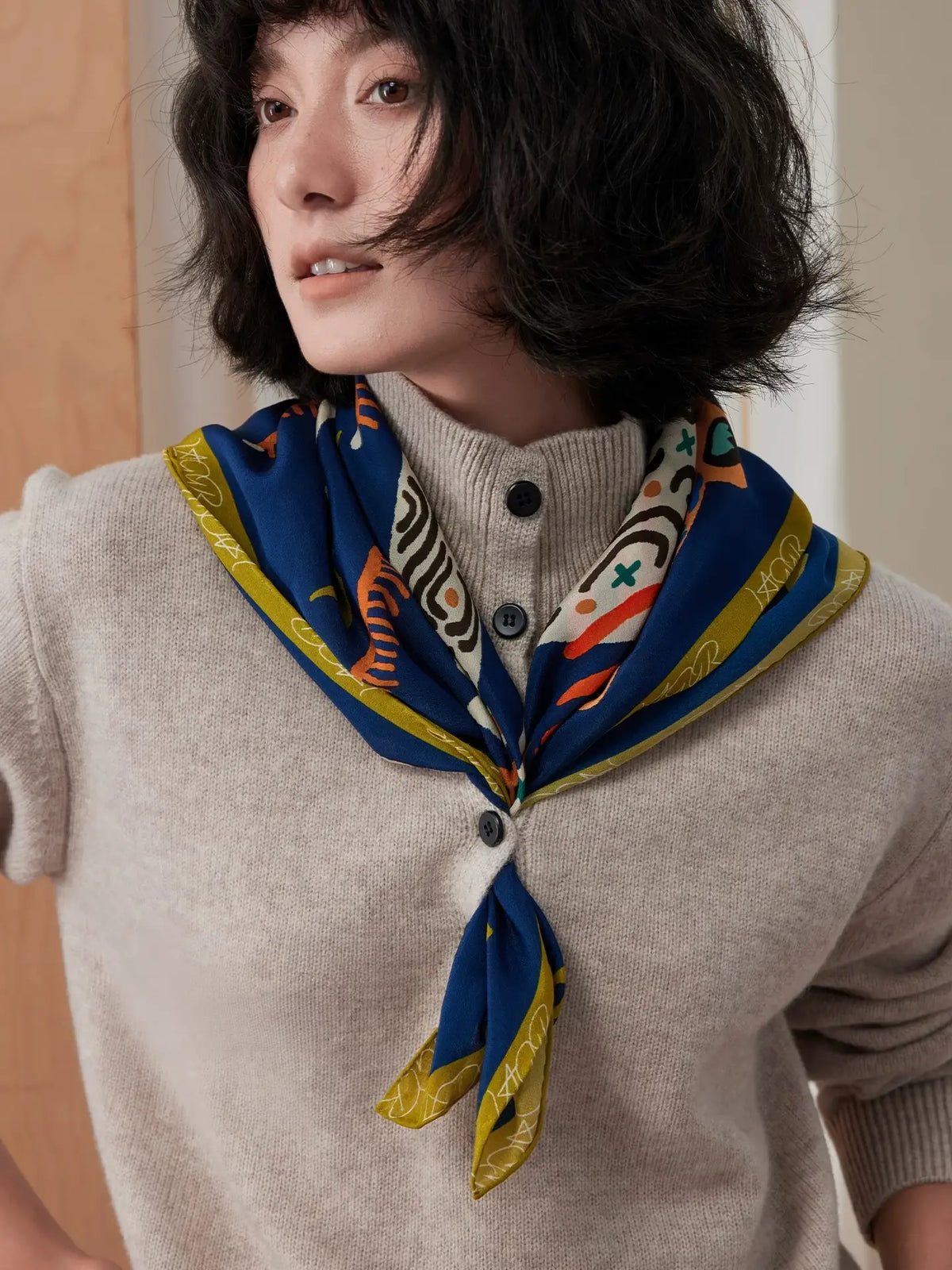Front view of a navy blue leopard floral mulberry silk scarf tied over a beige sweater