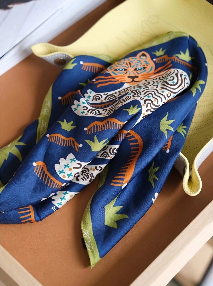 Navy blue leopard mulberry silk scarf folded on a tray, showing gold edging and fluid drape