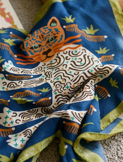 Close-up of a navy blue mulberry silk scarf with orange and ivory leopards and botanical details