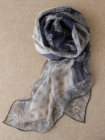 Navy and beige botanical paisley silk chiffon scarf displayed on fabric