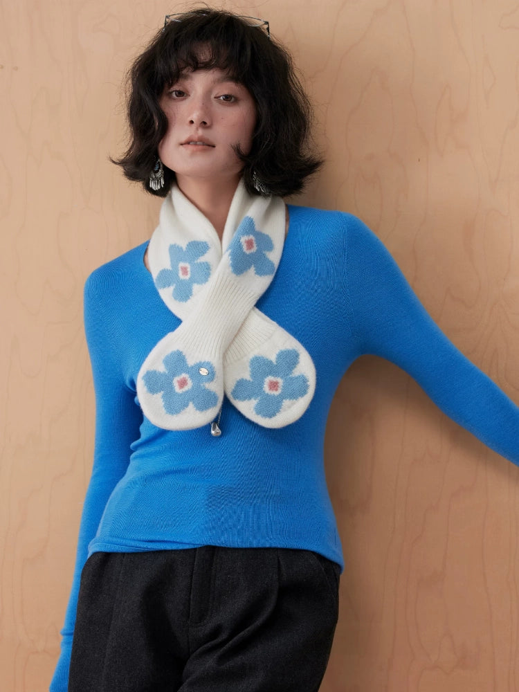 Front view of an ivory wool keyhole scarf with blue flowers, styled with a blue sweater and black trousers.