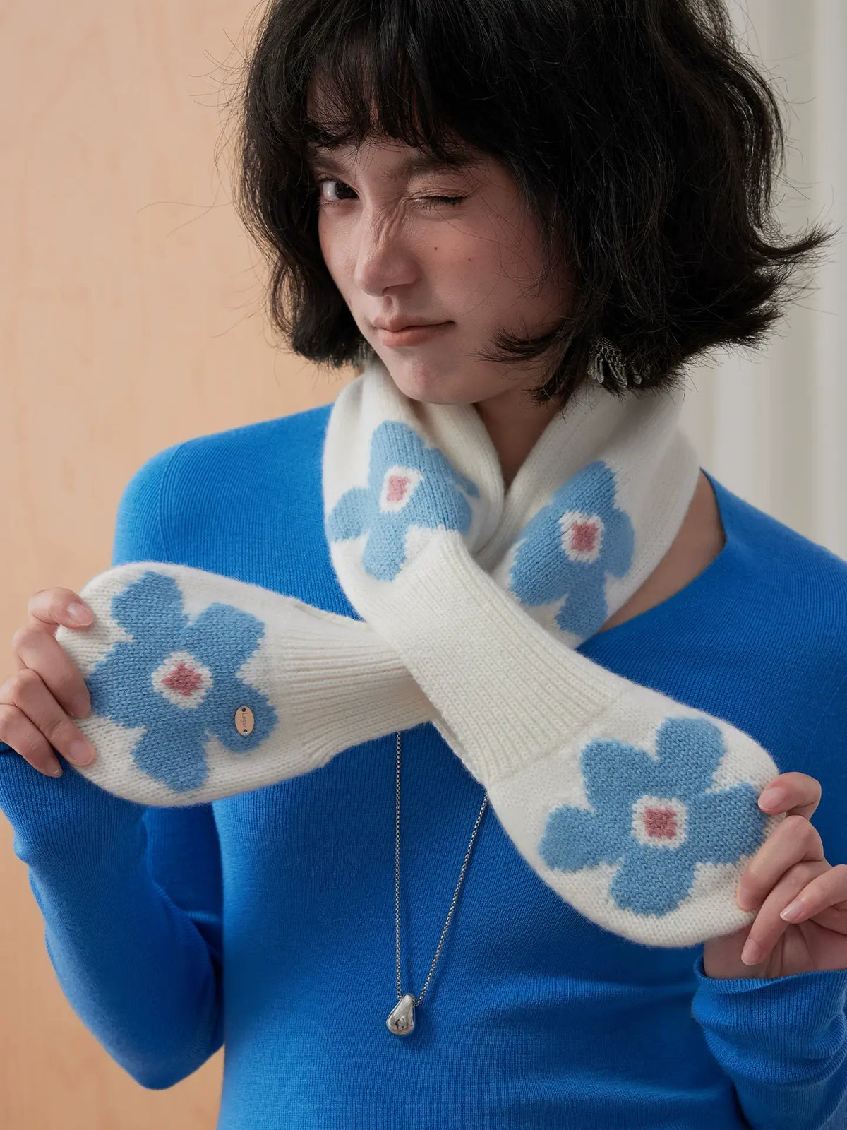 Close-up of an ivory wool keyhole scarf with blue flowers, with both rounded ends held out.