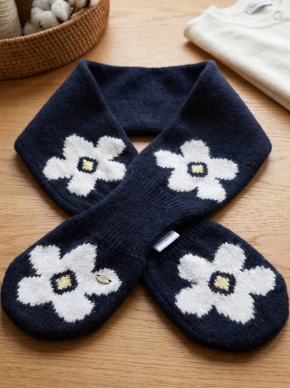 Navy wool keyhole scarf laid flat on a wooden surface, showing white flowers, crossed ends and knit texture.