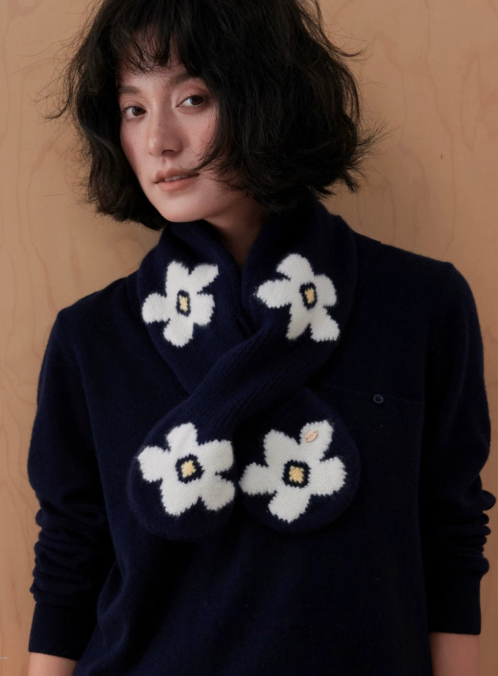 Close-up of a navy wool keyhole scarf with white flowers and rounded ends, worn with a navy sweater.