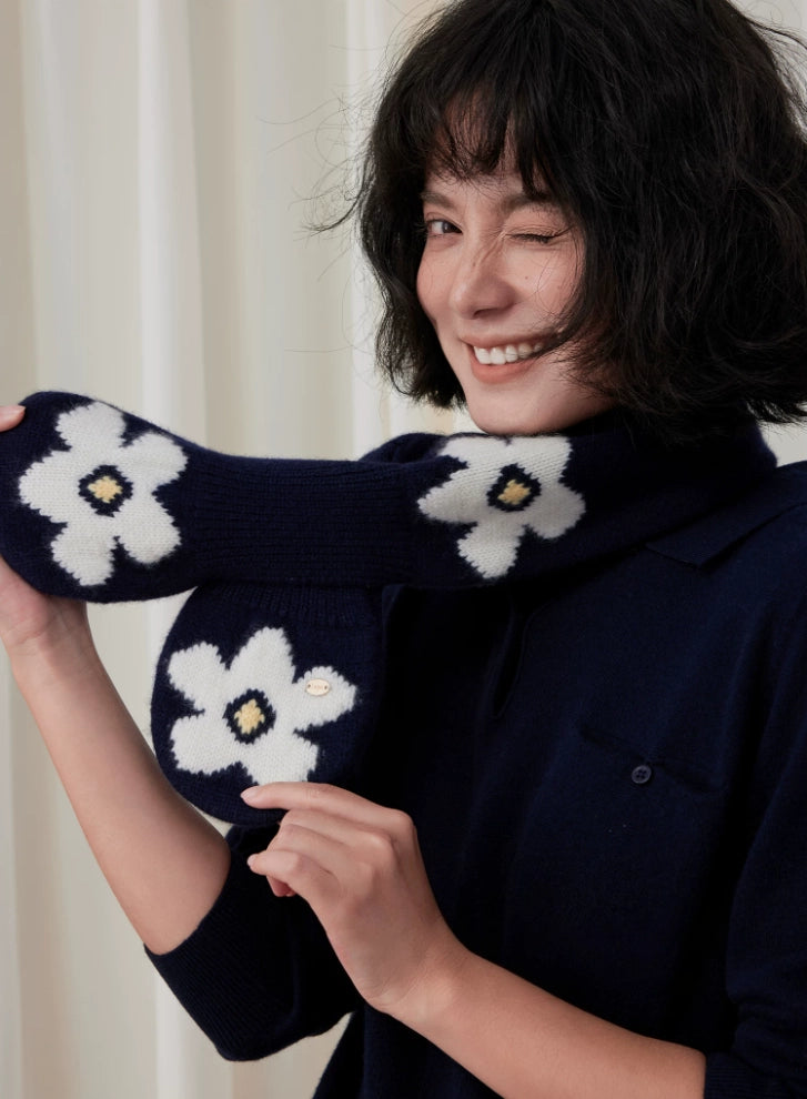 Model holding out a navy wool keyhole scarf to show its white flower motifs and rounded ends.