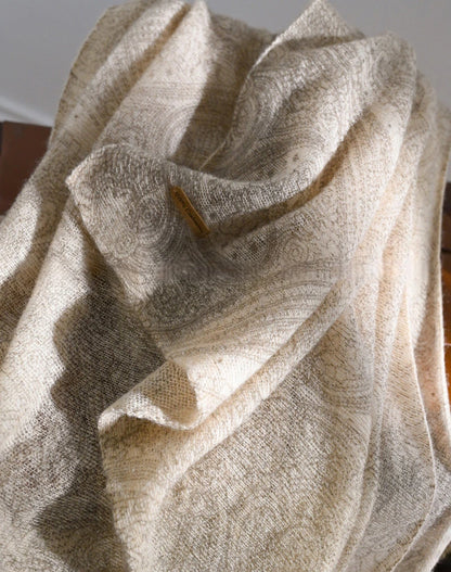 Oatmeal cashmere scarf gathered into soft folds, showing its subtle tonal pattern and fabric texture.
