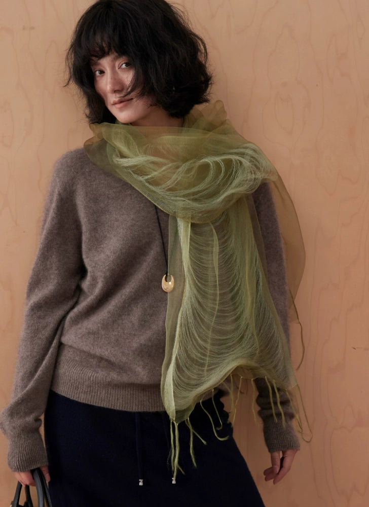 Woman styling a lightweight olive green silk scarf over neutral knitwear