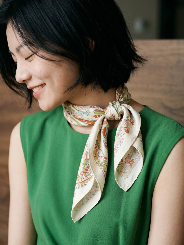 Woman wearing a pink beige elephant floral silk scarf in a side knot with a green top