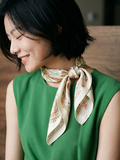 Woman wearing a pink beige elephant floral silk scarf in a side knot with a green top