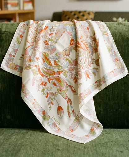 Pink beige mulberry silk scarf with elephant and botanical print draped over a green chair