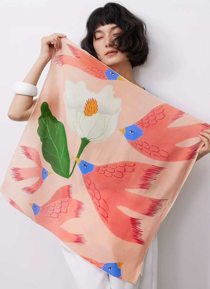 Model holding pink bird and floral mulberry silk square scarf in full design view