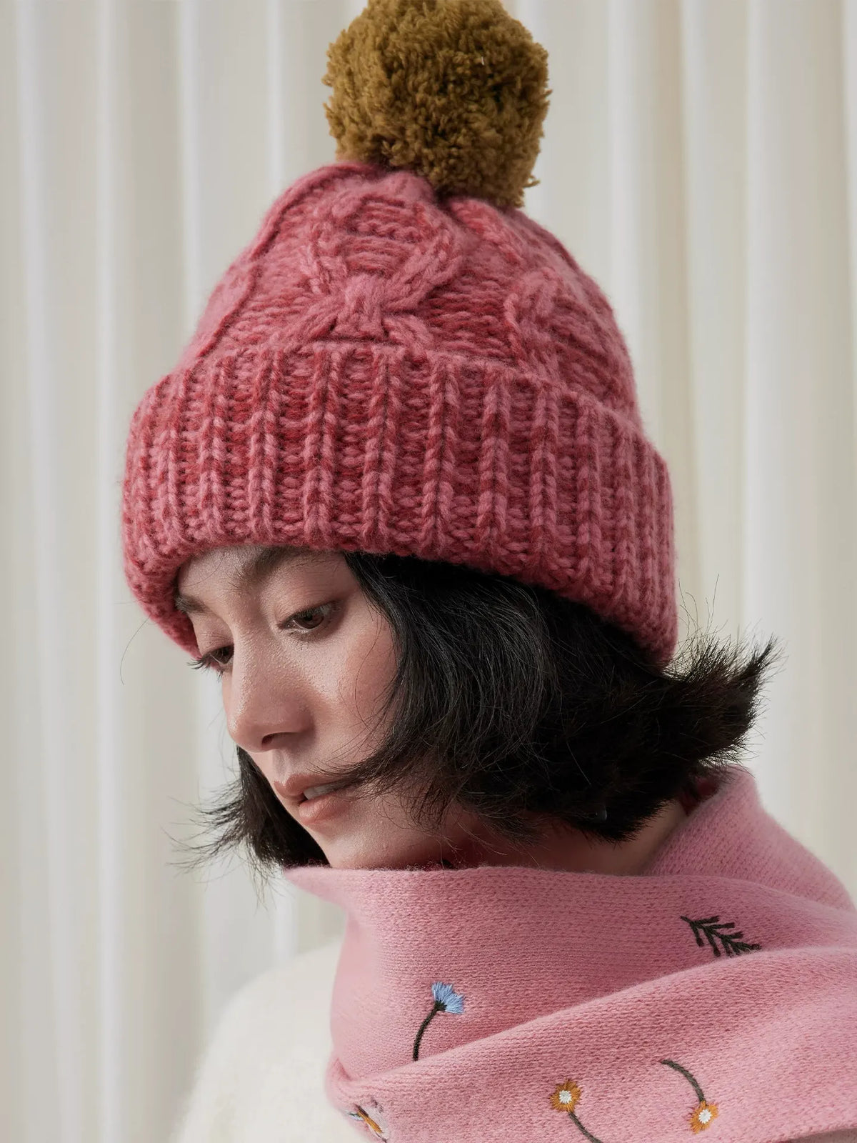 Side close-up of a dusty pink wool beanie, showing raised cable stitches and a wide ribbed cuff.