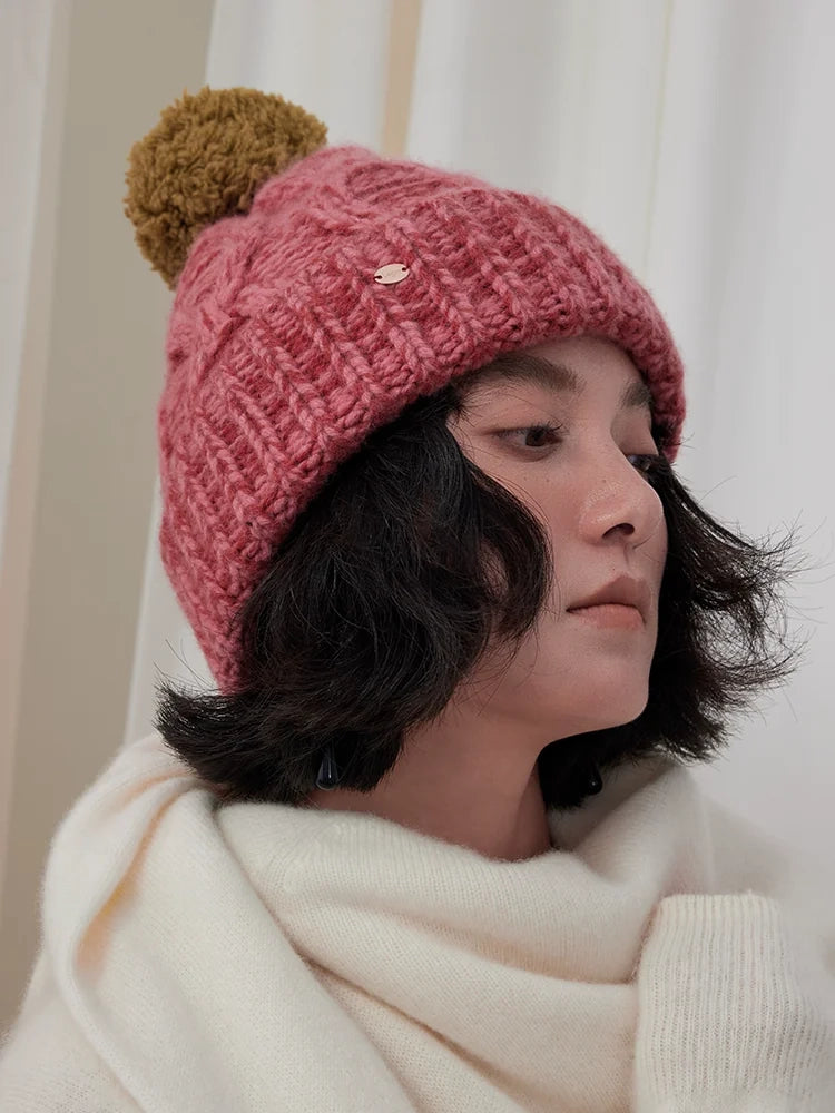 Side profile of a model wearing a dusty pink cable knit pom pom beanie with a cream scarf.