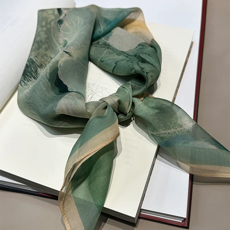 Plant-dyed mulberry silk square scarf in green floral design, tied and styled on book surface
