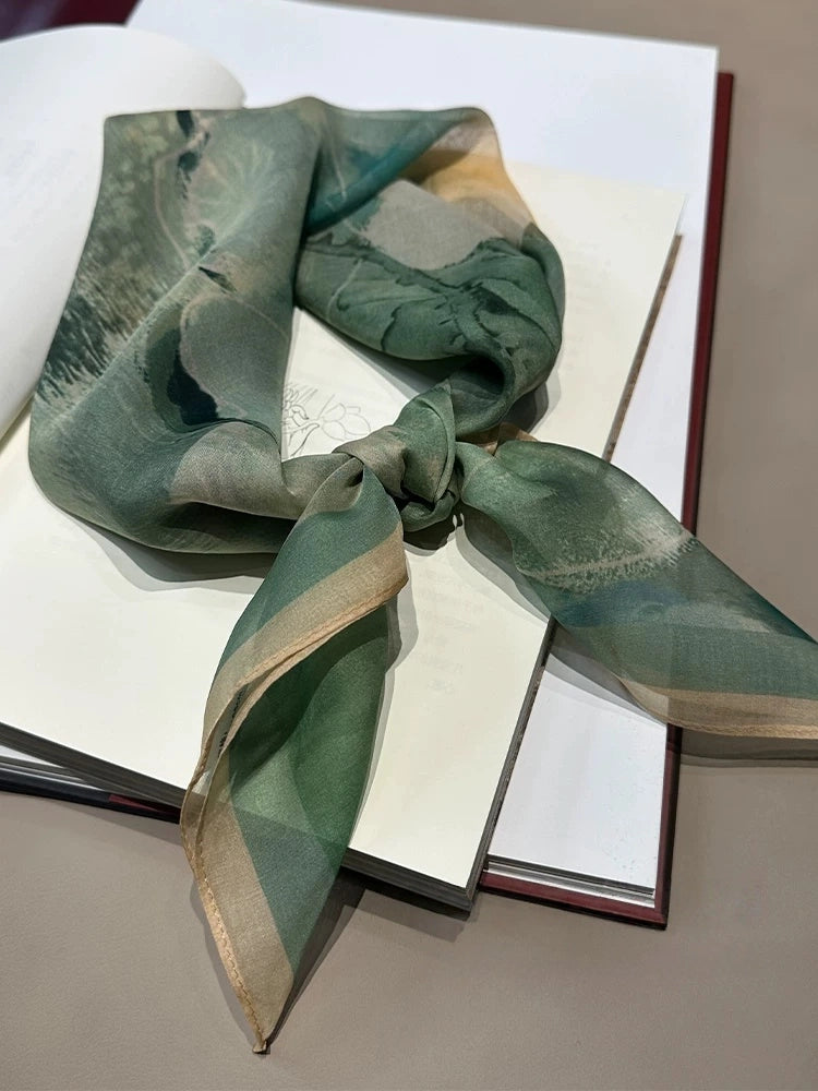 Lightweight silk square scarf in green floral pattern, folded and styled on book background