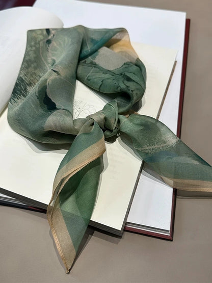 Lightweight silk square scarf in green floral pattern, folded and styled on book background