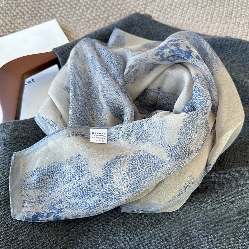 Elegant blue plant-dyed silk scarf with soft ink-wash pattern arranged on a light tabletop