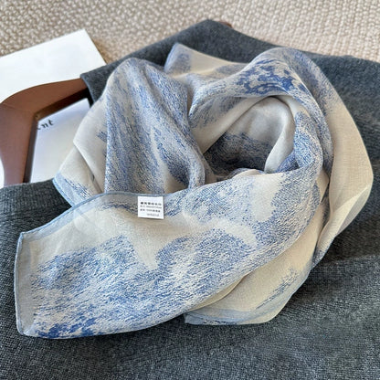 Elegant blue plant-dyed silk scarf with soft ink-wash pattern arranged on a light tabletop