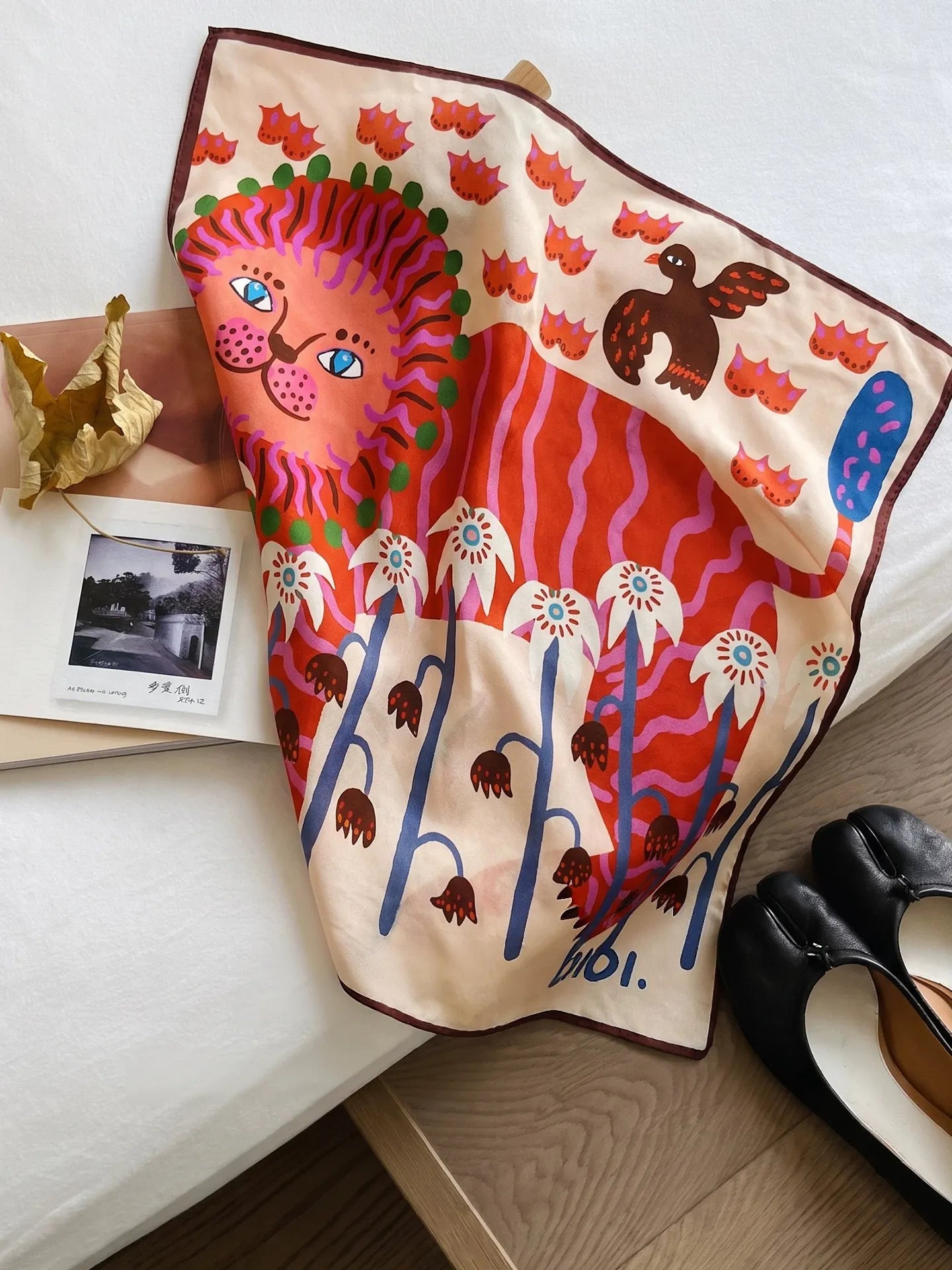 Cream mulberry silk square scarf with a coral lion and whimsical botanical print displayed on a chair