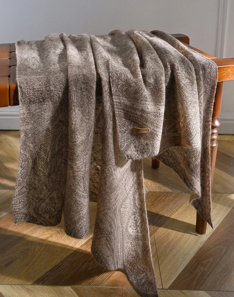 Plum brown lightweight cashmere scarf draped over a wooden chair, with paisley motifs along the folds.