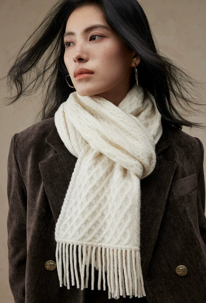 Close-up of a pure white cable knit scarf knotted at the neck, showing its diamond knit pattern and fringe.