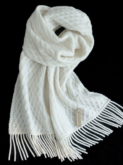 Pure white cable knit scarf loosely knotted on a black background, showing the knit texture and fringed ends.