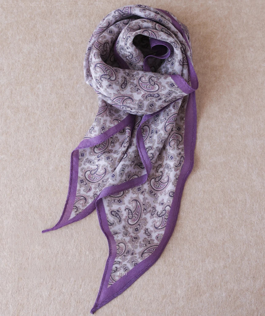 Purple paisley silk wool diamond scarf arranged on a neutral fabric background