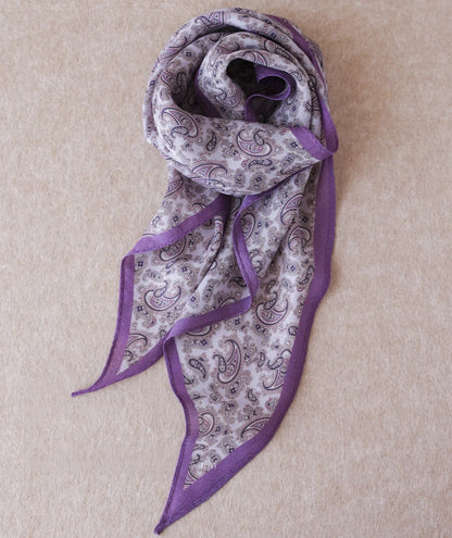 Purple paisley silk wool diamond scarf arranged on a neutral fabric background