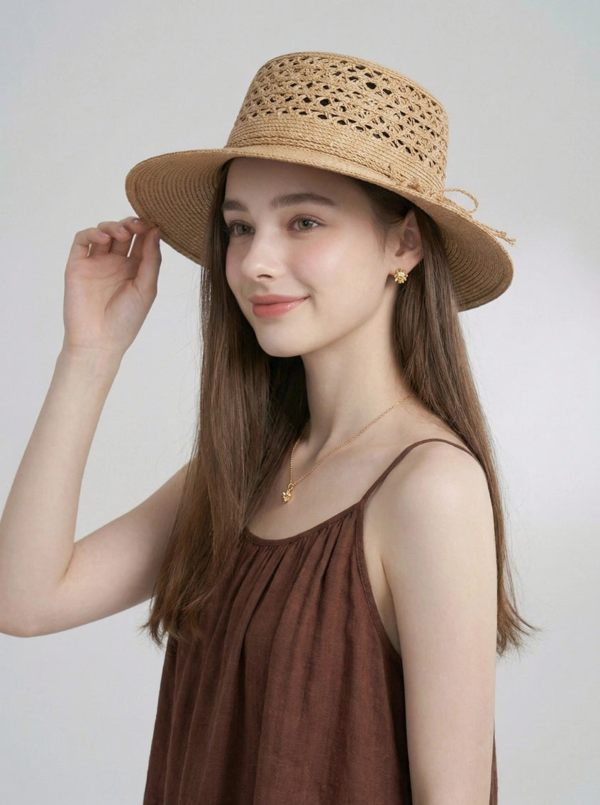Model wearing beige raffia straw boater hat with wide brim and open weave crown.