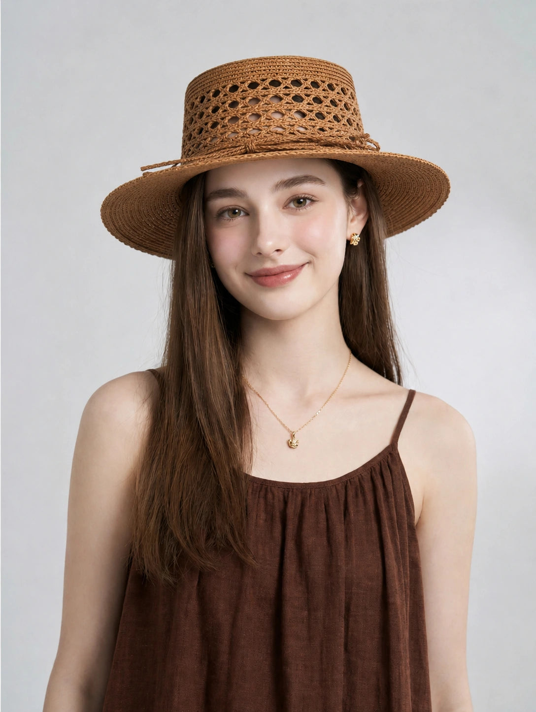 Model wearing antique bronze raffia boater hat with hollow woven crown.