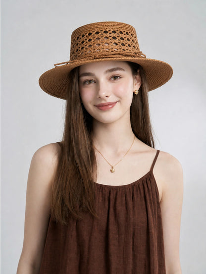 Model wearing antique bronze raffia boater hat with hollow woven crown.