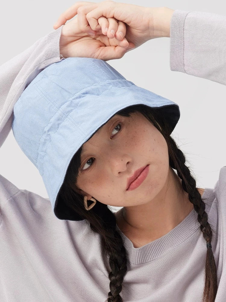 Woman styling a light blue reversible bucket hat made from a breathable cotton linen blend