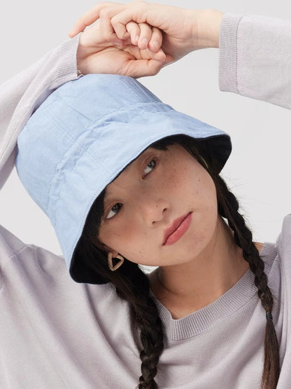 Woman styling a light blue reversible bucket hat made from a breathable cotton linen blend