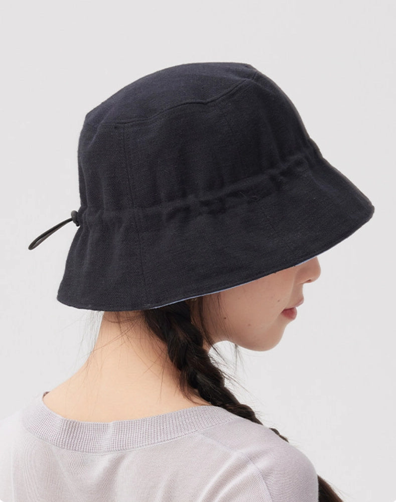 Rear side view of a black navy reversible bucket hat with an adjustable inner drawstring