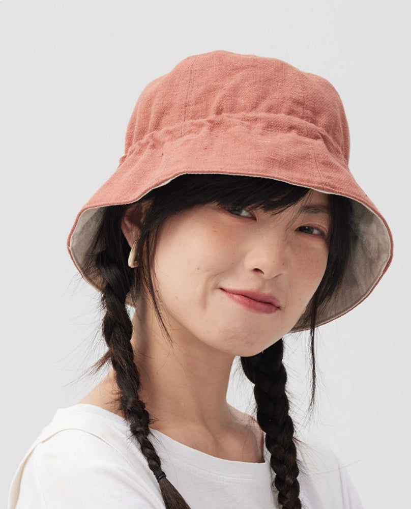 Front view of a woman wearing an orange pink reversible cotton linen bucket hat with a soft brim