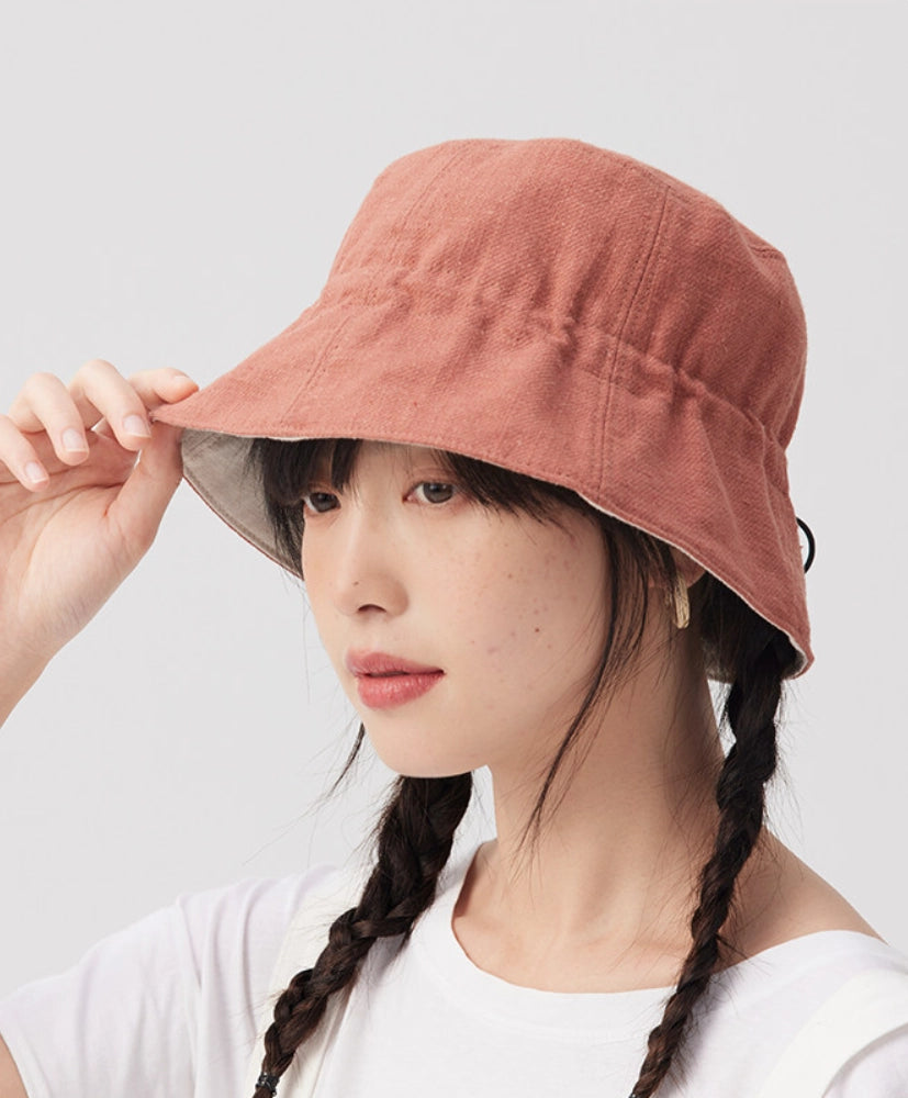 Woman adjusting the brim of an orange pink cotton linen bucket hat for casual summer styling