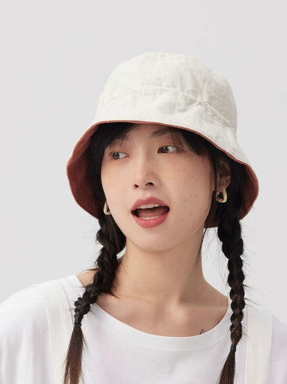 Woman wearing the light neutral side of a reversible bucket hat with a contrasting orange pink lining