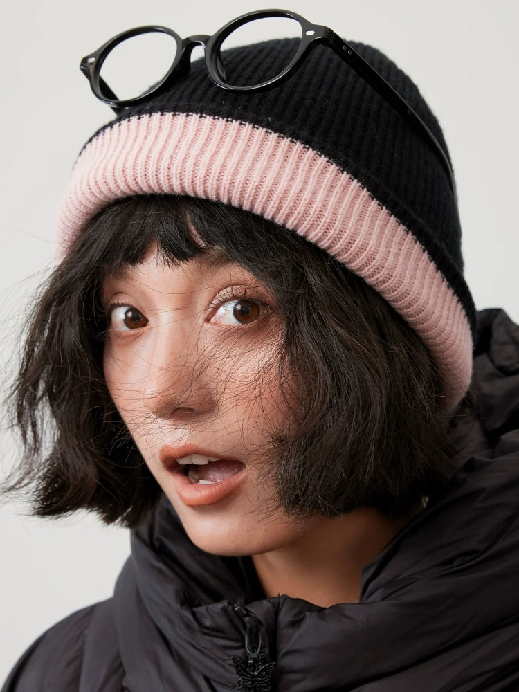 Black rib-knit wool beanie with a cherry blossom pink fold-over cuff and glasses resting on the crown.
