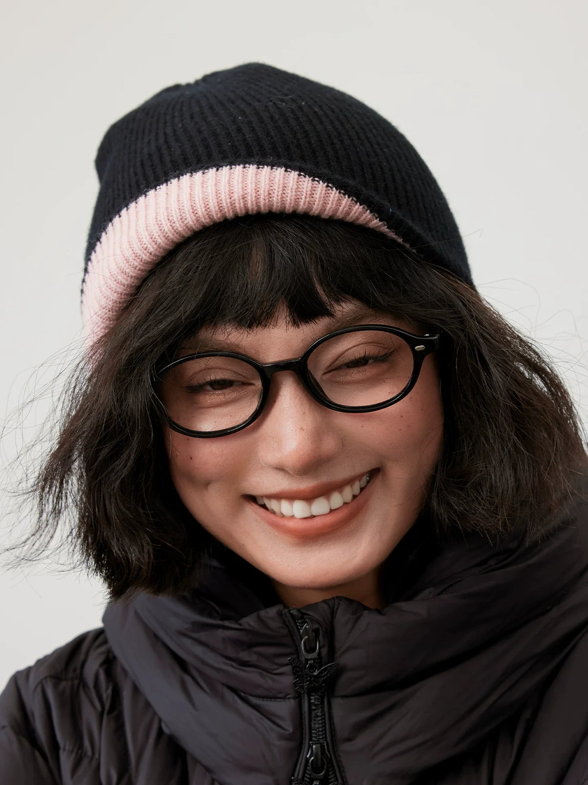 Front view of a black reversible wool beanie with a cherry blossom pink cuff, worn by a smiling model.