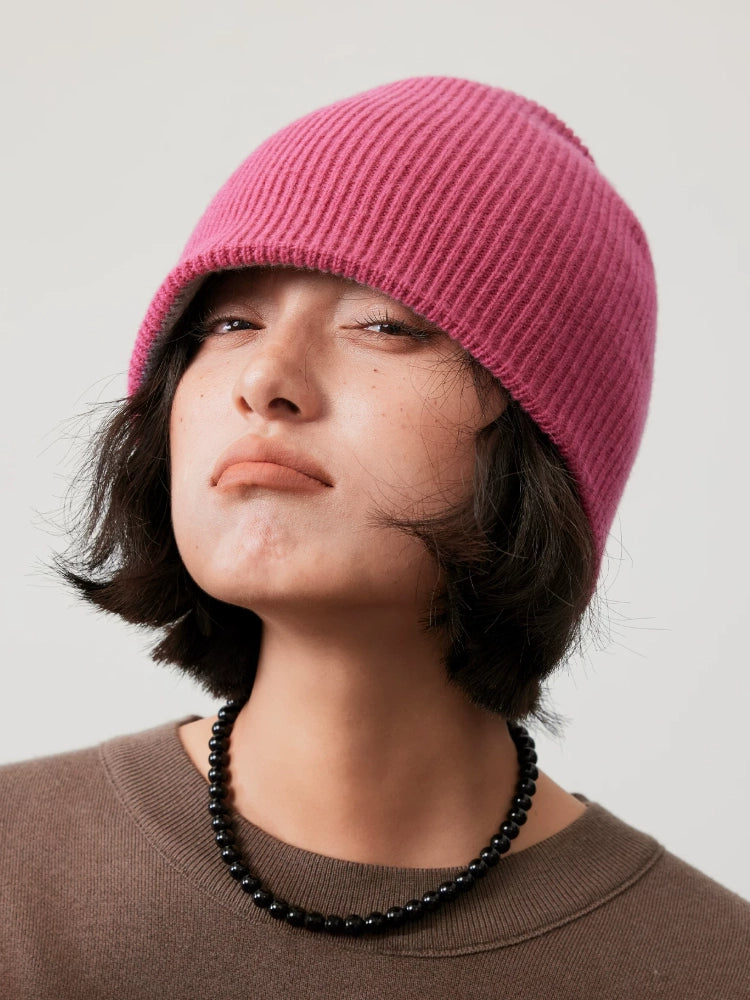 Front view of a model wearing the rose pink side of a reversible rib-knit wool beanie.