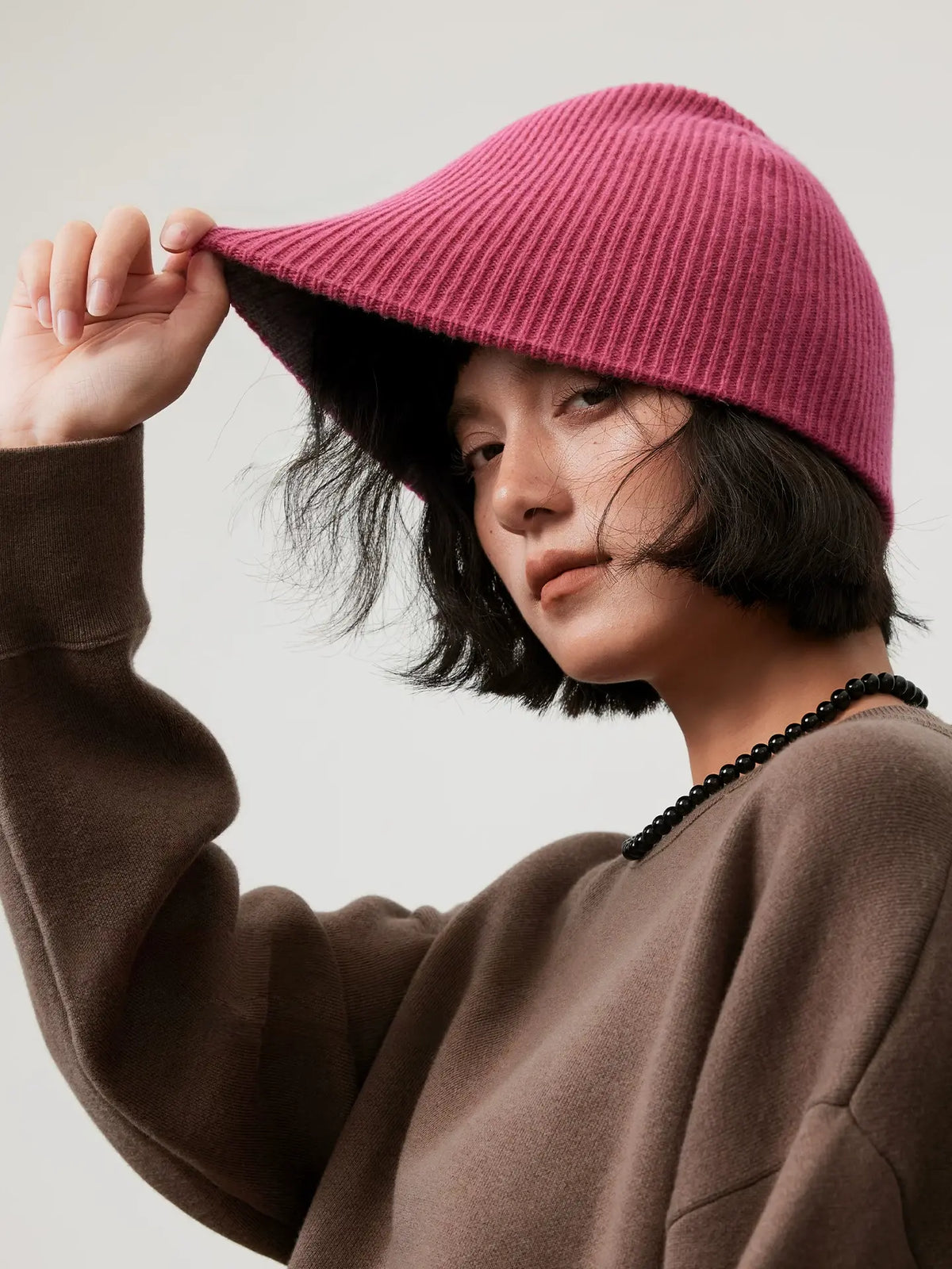 Model stretching the edge of a rose pink wool beanie outward, showing its flexible rib-knit construction.