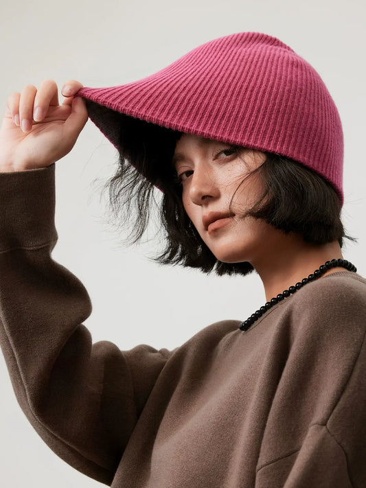 Model stretching the edge of a rose pink wool beanie outward, showing its flexible rib-knit construction.