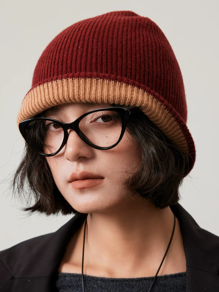 Close-up of a rust brown rib-knit wool beanie with a camel fold-over cuff, worn with black glasses.