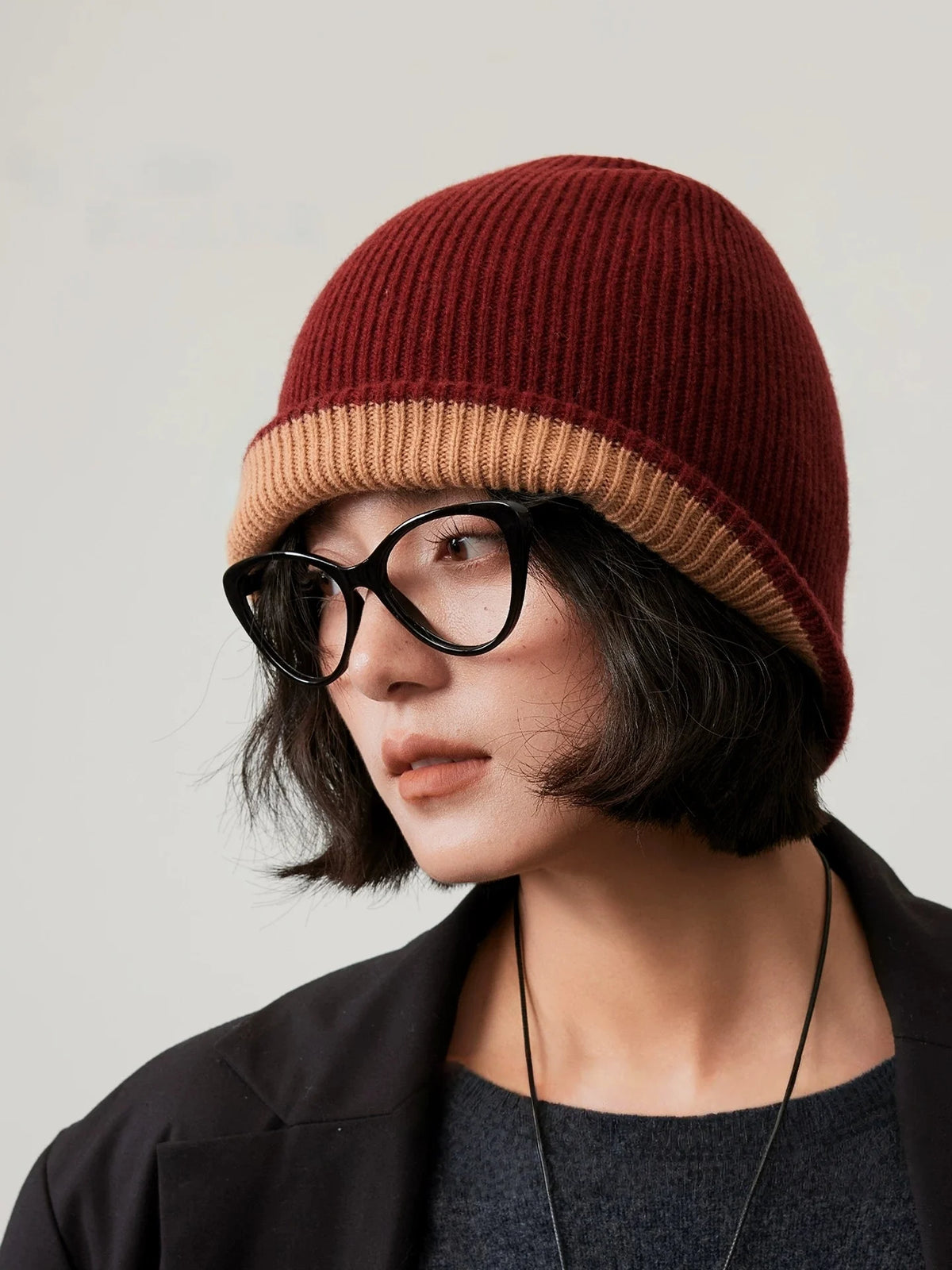 Three-quarter view of a rust brown wool beanie with a camel cuff, styled with a black blazer.