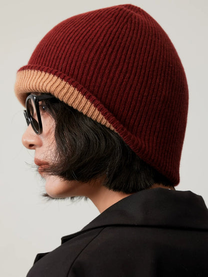 Side view of a rust brown rib-knit wool beanie with a camel edge, showing the rounded crown.