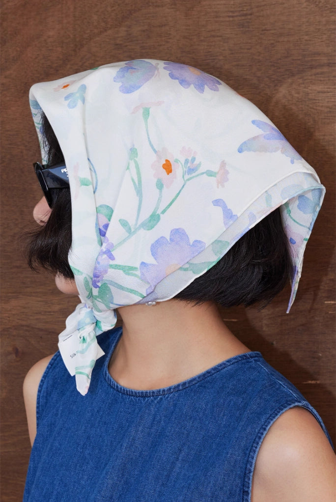 A square silk scarf with a watercolor floral design worn as a headscarf to showcase how it is styled.