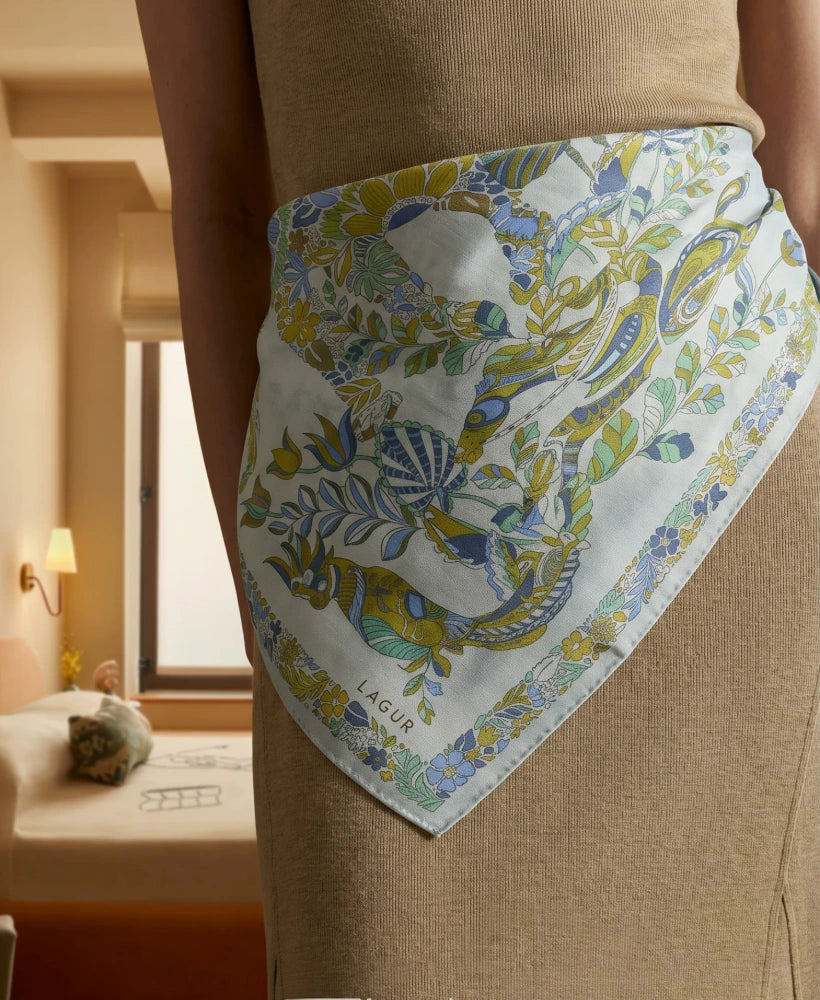 Snow Mountain Blue elephant floral silk square scarf styled as a waist accent over neutral trousers