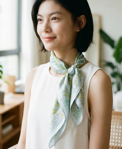 Woman styling a Snow Mountain Blue elephant floral silk scarf in a neat side neck kno