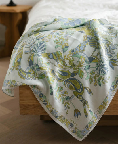 Snow Mountain Blue mulberry silk scarf with elephant and botanical print draped over a wooden surface