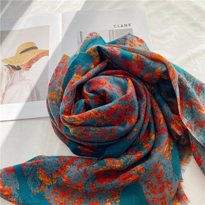 Teal and red artistic wool scarf arranged in a spiral beside a fashion magazine